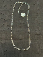 Silver chain with a coin on a textured black fabric background
