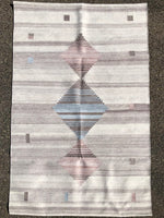 This hanwoven rug was made from recycled water bottles.  It has a background of brownish grey tones with thee diamonds, one being light blue and two a brownish mauve.