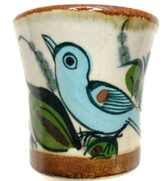 Ken Edwards small drinking cup with brown rim .   It is natural grey clay color background with birds, butterflies, and leaves in blue, green, black and brown on the outside.