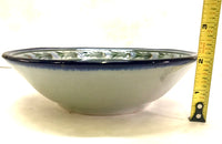 Ken Edwards Collection stoneware soup or cereal bowl with blue rim. It is natural grey clay color background with birds, butterflies, and leaves in blue, green, black and brown on the face of the plate.