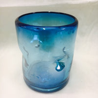 Hand blown glass in solid aquamarine color with a pinched effect on the outside for secure handling while drinking.  Very comfortable.