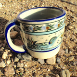 Ken Edwards Collection series coffee mug.   It is natural grey clay color background with birds, butterflies, and leaves in blue, green, black and brown on the outside.