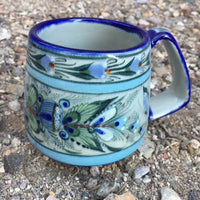 Ken Edwards Collection Series truncated coffee mug with  green, two shades of blue and brown flowers, birds, and butterflies decorated on the side or inside on bowls or plates