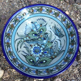 Ken Edwards Collection stoneware soup or cereal bowl with blue rim.  It is natural grey clay color background with birds, butterflies, and leaves in blue, green, black and brown on the face of the plate.