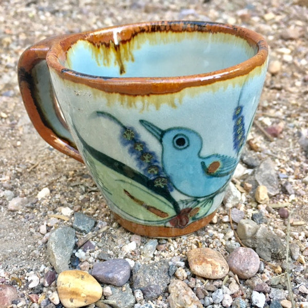This beautiful mug is natural grey clay color with brown rim and handle and the outside is decorated with blue birds and green leaves.